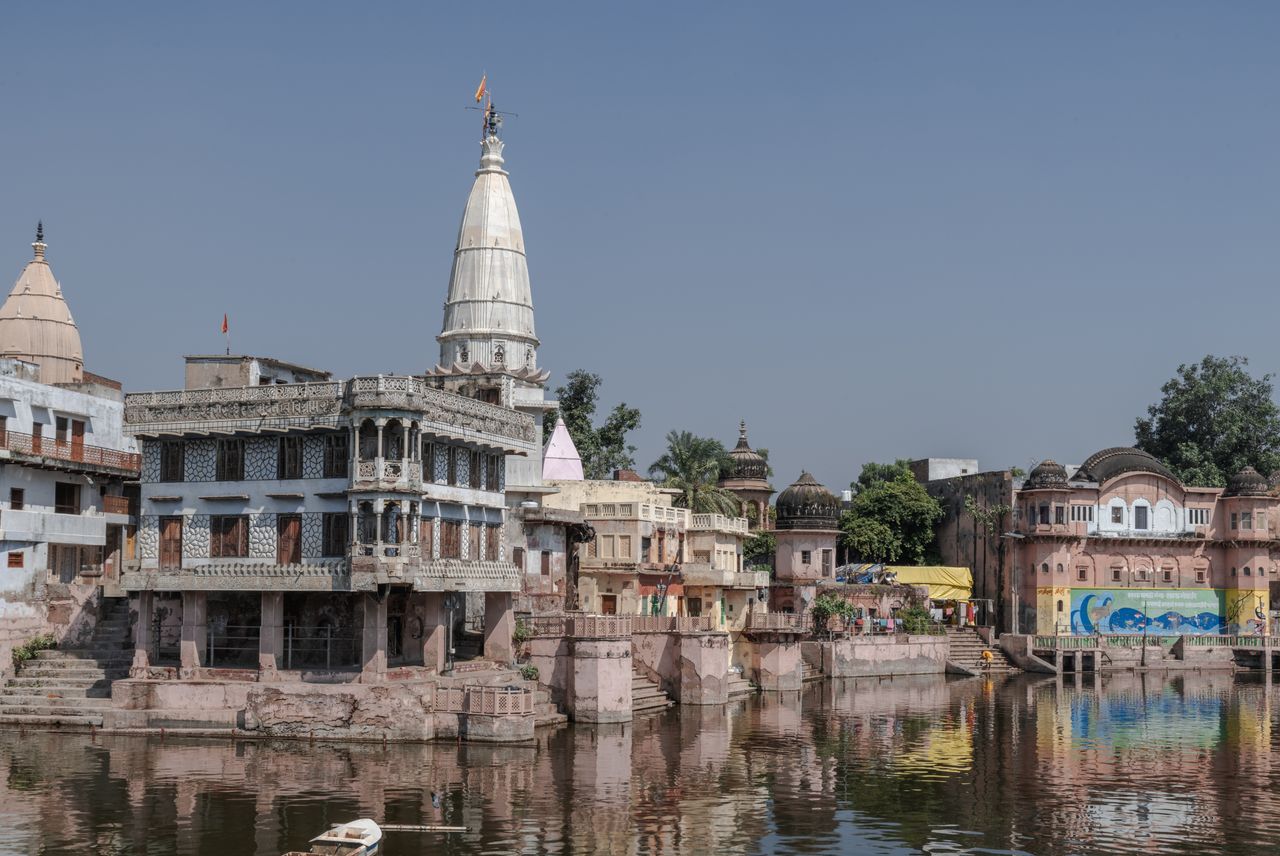 Scenic view of Govardhan's historic buildings reflecting in a serene water body in Uttar Pradesh, India.